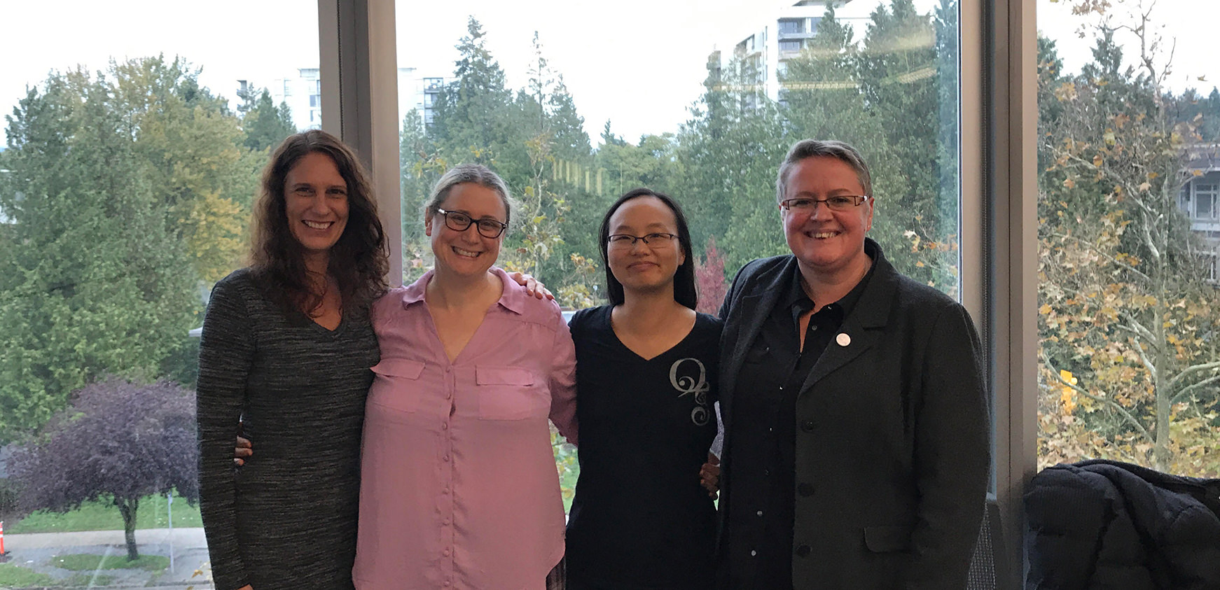 Photo of: Dr. Erin Michalak, Dr. Michelle Walks, Dr. Iva Cheung, and Beverley Pomeroy, standing together in front of a window.