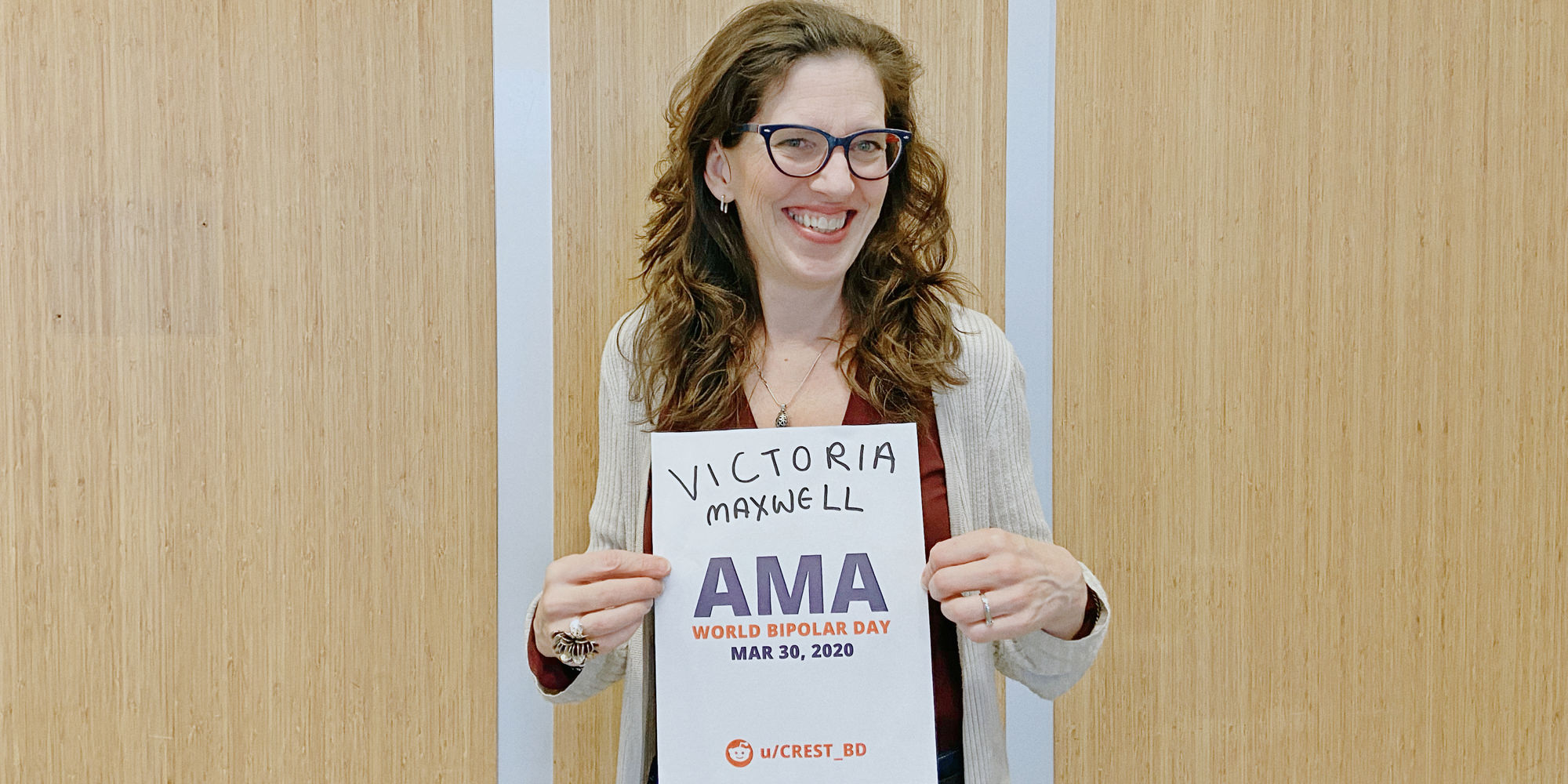 Victoria standing in front of wood panels, smiling and holding a proof sign.