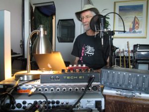 Bruce seated in front of editing equipment and wearing a hat.