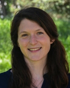 Julia, from the neck up, smiling. She's outside against a blurred green background.