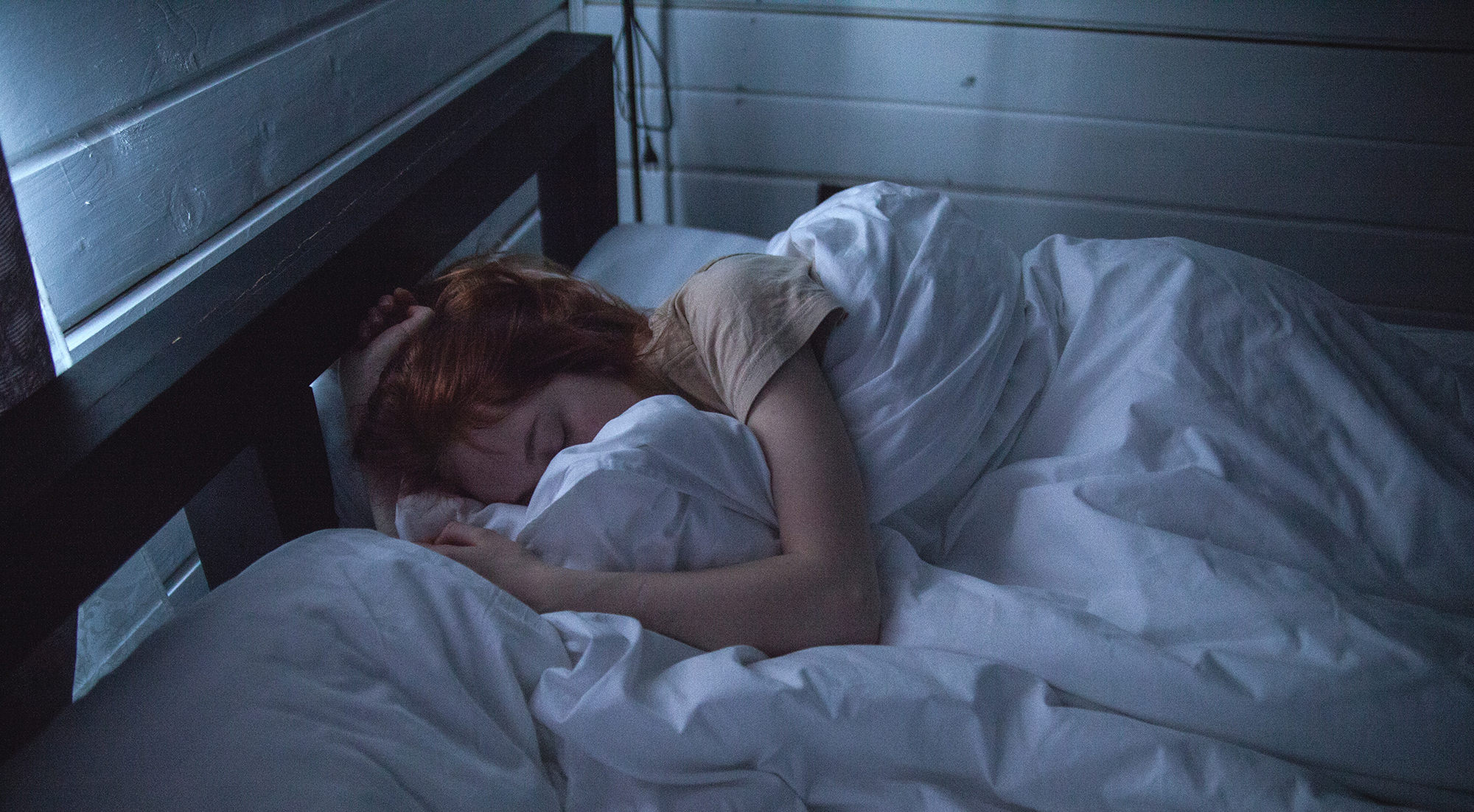 A person with red hair curled upin bed sleeping.