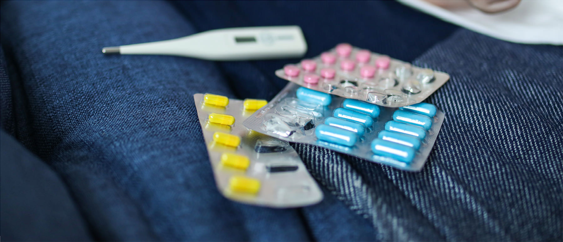 Three packs of pills on denim, probably from someone's jeans, and a thermometer.