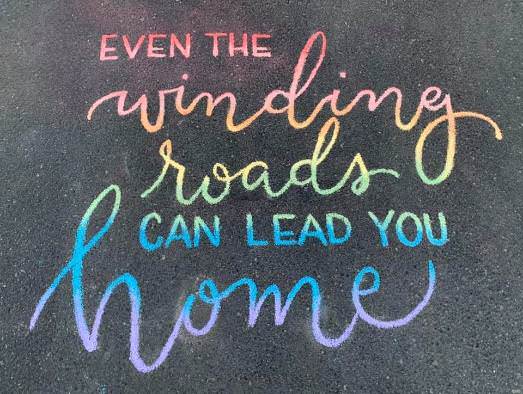 Chalk art done in rainbow colours on a road, saying 'Even the winding roads can lead you home,' reflecting Raymond's sentiments on aging well with bipolar. 