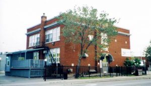 The outside of the Shepherds of Good Hope building, a two-story brick building with a small yard and a tree in front.