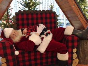 Raymond as Santa Clause! He's lying down on a black-and-red checked chair with a small baby sleeping on his chest.