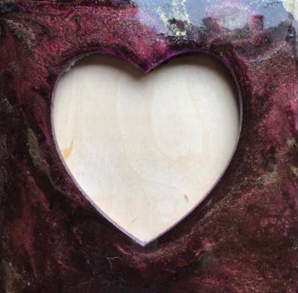 A cut-out of a heart in a frame. The frame is dark purple and marbled with bright green sparkles and different shades of purple.