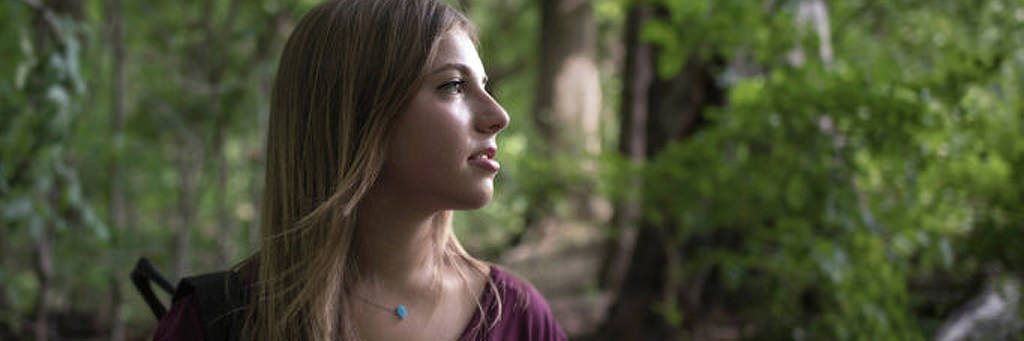 Tera is shown in profile in a forest. She is looking out thoughtfully and is wearing a burgundy shirt and turquoise necklace.