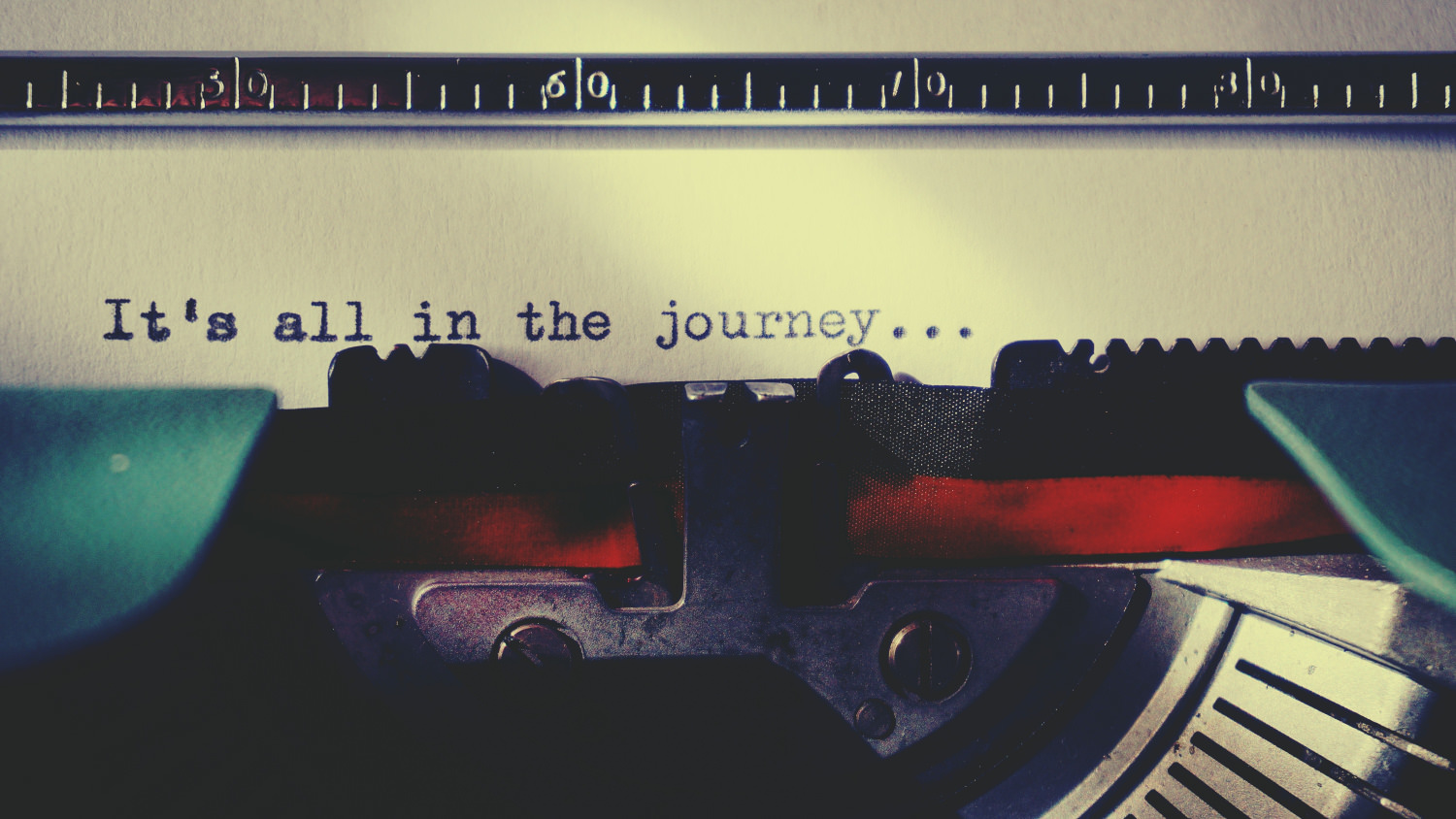 A close-up picture of a blue typewriter, showing the bottom of the page. Written on it is, 'It's all in the journey...' .