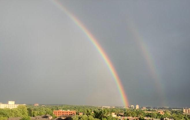 A cloudy sky with two massive rainbows arcing above a town.