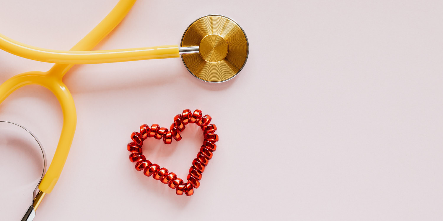 A beaded heart laying on a pale pink table, next to a yellow doctor stethoscope.
