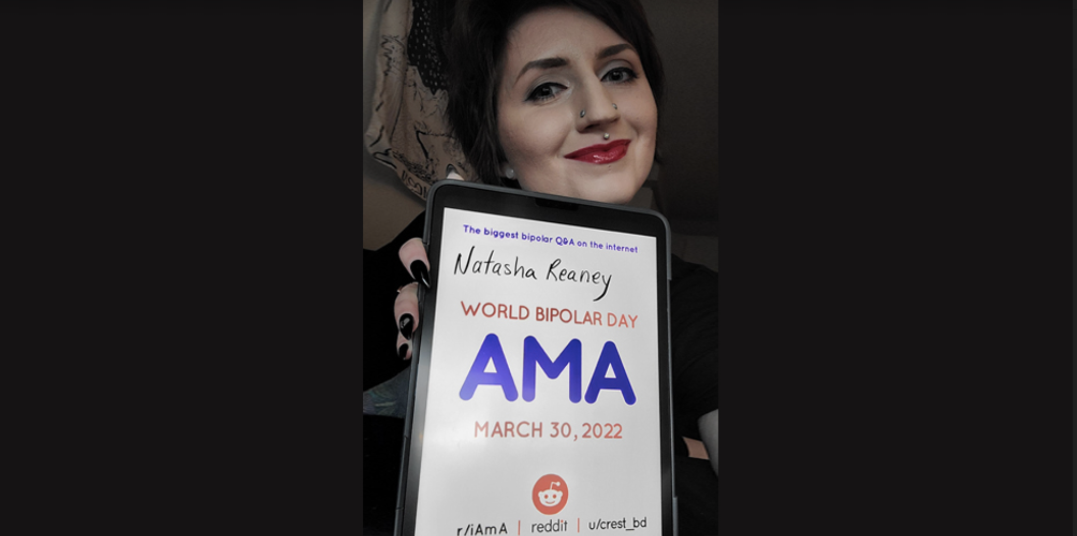 Natasha is taking a selfie. She has dark black hair, which is in a bun on the top of her head. In front of her is the AMA sign.