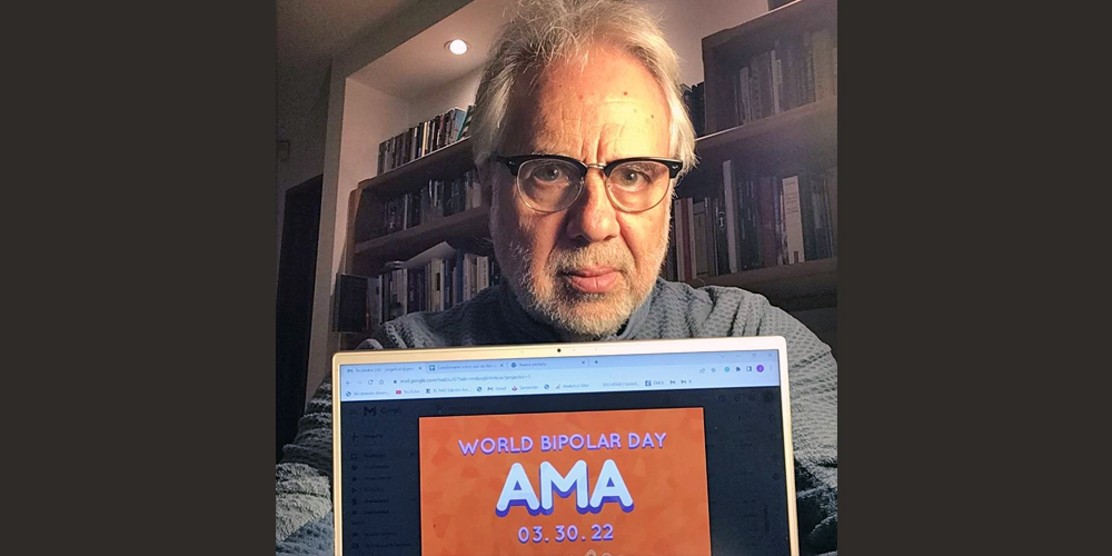 Jorge is sitting in front of a wall filled with bookshelves. He has white hair and a salt and pepper beard. He is wearing wire framed glasses with a black piece. In front of him is a tablet with the AMA banner on it.