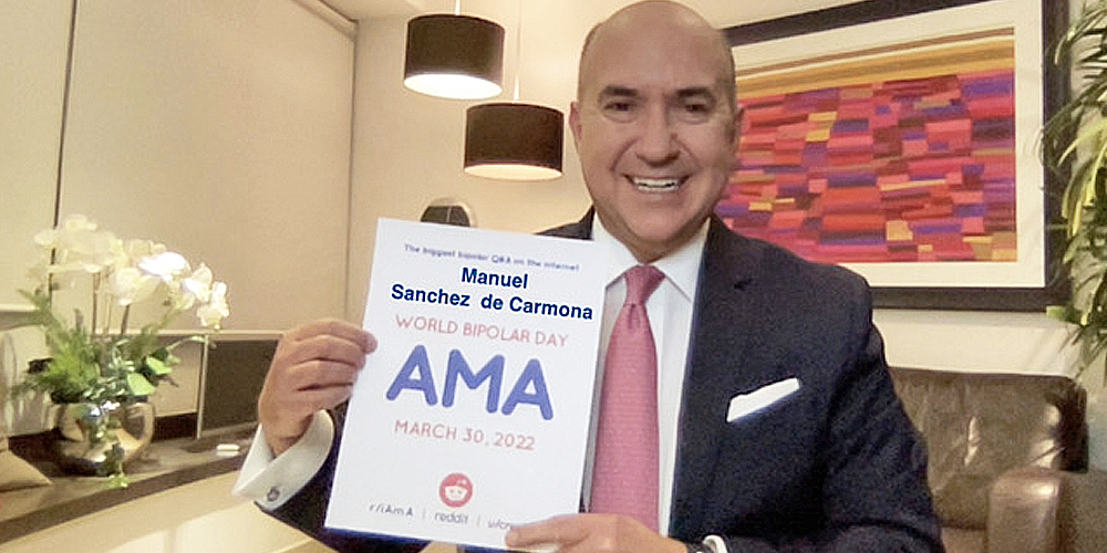 Manuel is in an office with a red abstract painting behind him. He is bald and Caucasian. He is wearing a dark blue suit, with a white button up and salmon pink tie. He is smiling and holding the AMA poster with both hands.