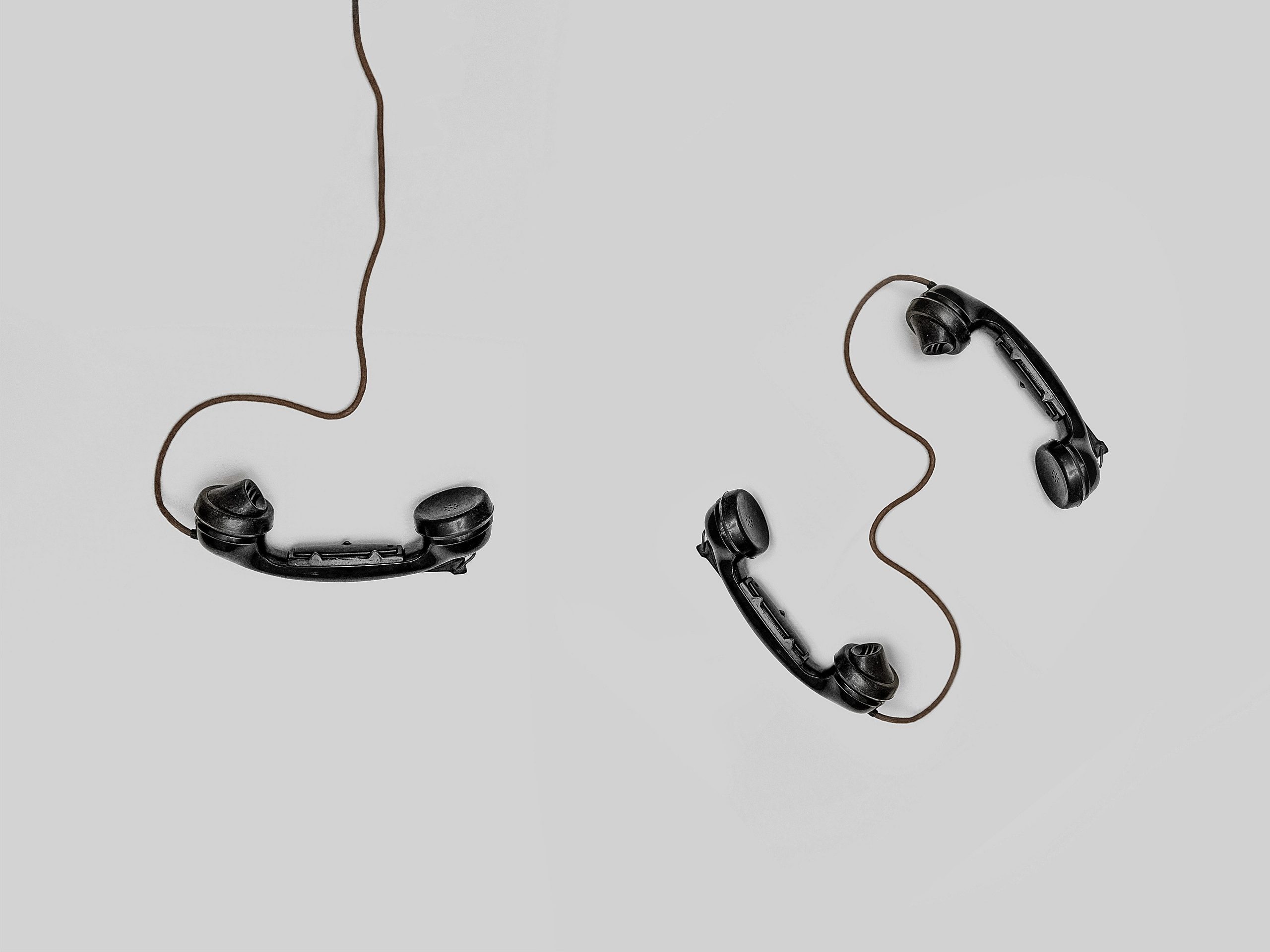 The background is white. Three phones lie haphazardly on the white background, with cords trailing out of the picture. 