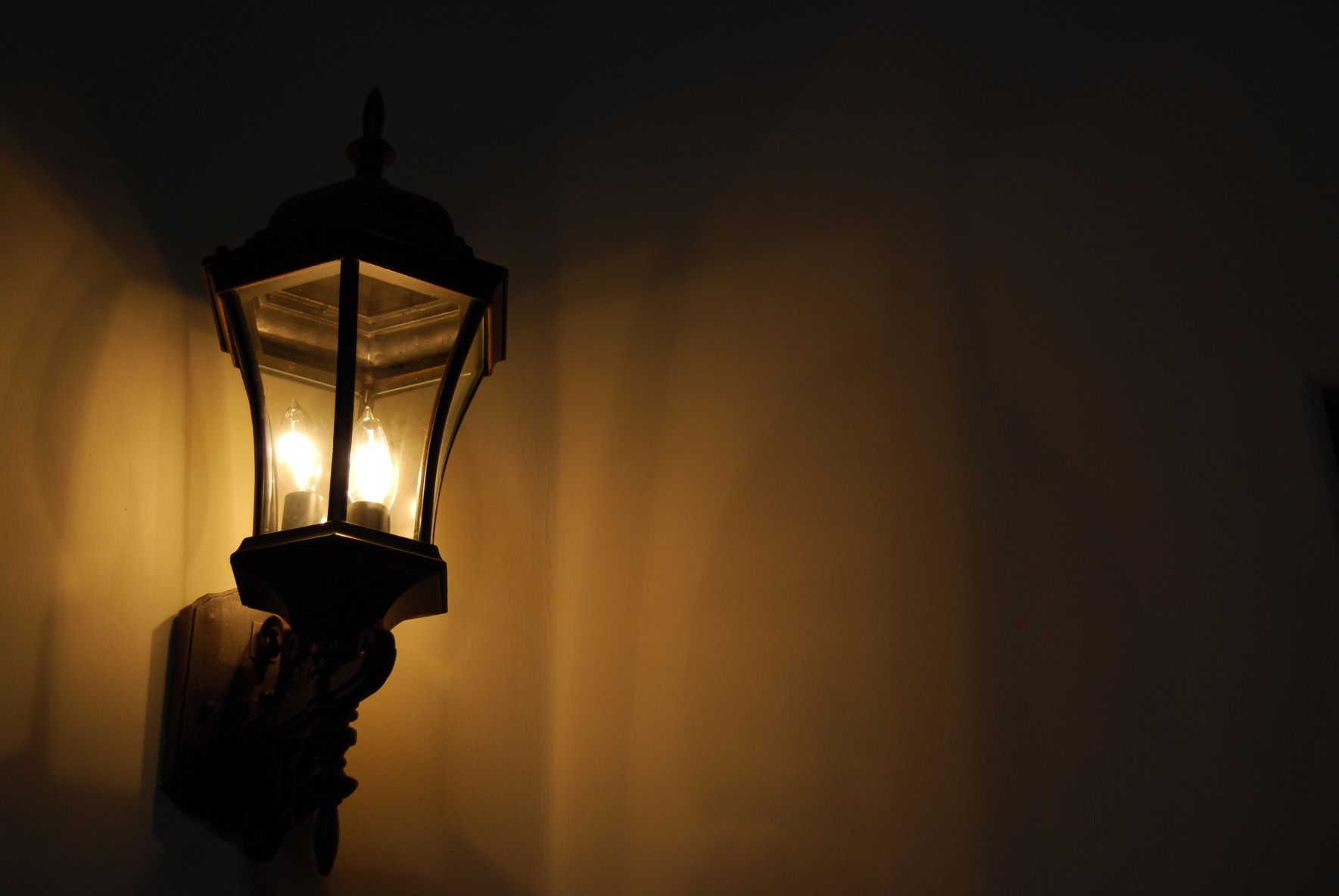 Image is of a white wall in a dark room. On the left side of the image is a lantern lighting the room.