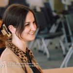 A woman wearing a tan jacket with a leapord print colour is looking to the right and smiling. Her brown hair is tied back in a hair clip. She is sitting in a boardroom. The CREST.BD logo runs along the bottom of the image.